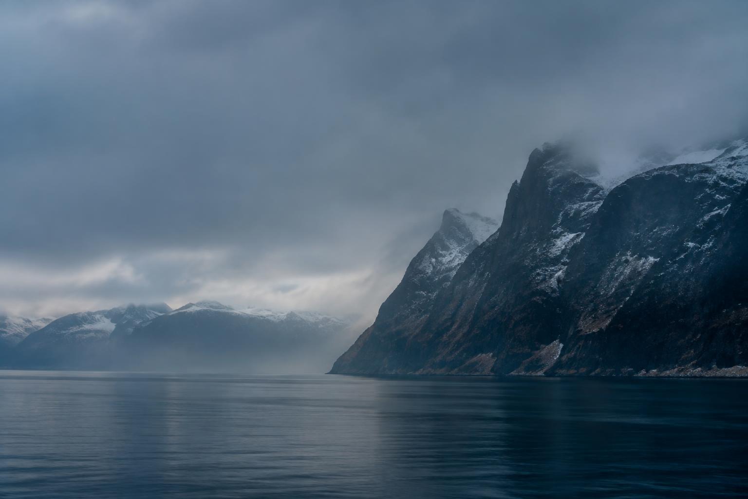 Snow-covered fjord cliffs seen from the sea in low winter light